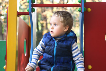 A little boy with blond hair,sits on an attraction and looks surprised to th side.Active...
