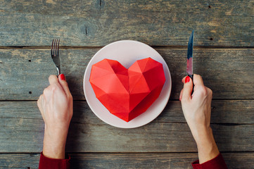 Young woman ready to eat paper volume heart on the plate on rustic wooden background