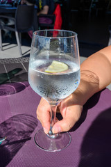 Drinking cold mineral water with bubbles, served in wine glass with ice cubes and lemon