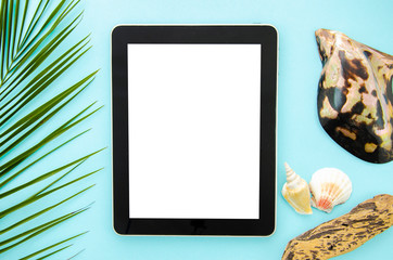 Flat lay mockup tablet over tropical palm leaf and seashells on a pastel blue background. Top view with copy space on screen
