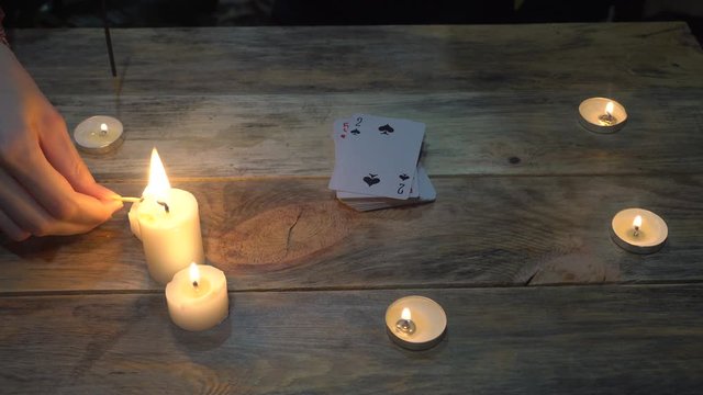Fortuneteller's female hand, lights candles on the background of fortune-telling cards.