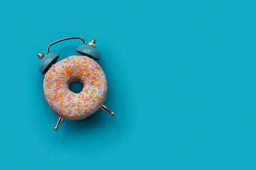 Pink alarm clock donut on blue background. Breakfast time or minimal concept. Copy space. Top view