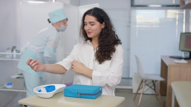 Sequence of shots of nurse in medical uniform applying tourniquet, disinfecting skin and taking venous blood from arm of young beautiful Caucasian woman