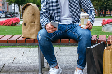 Unrecognizable young man looking at the cell phone sitting on a park bench