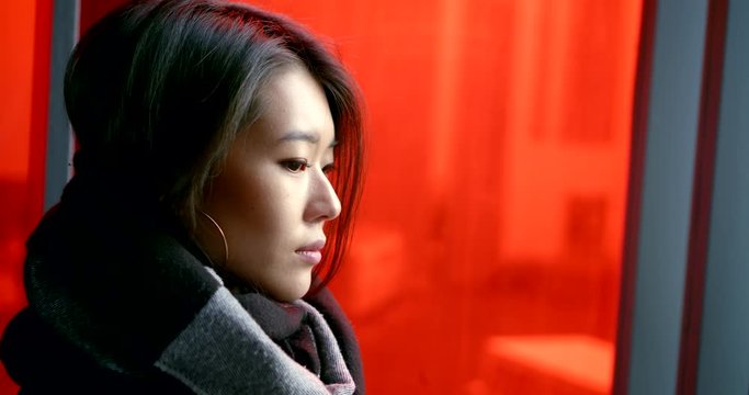 Close-up portrait of an Asian girl with short dark hair, wearing a scarf around her neck-Snood, she is on the background of a red window.