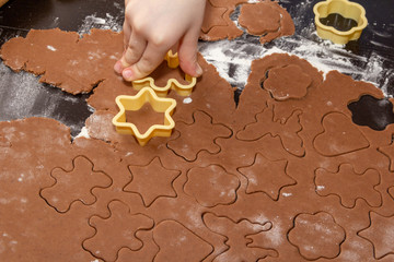 Cutting figures from the dough using special stencils for making ginger Christmas cookies. Children's hands close-up. Home, family prepare for the holidays concept