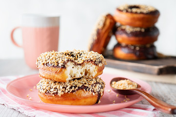 Stack of donuts with chocolate glaze and waffle crumbs on a pink plate with a pink striped napkin, a pink mug, and wooden spoon on a light gray background.