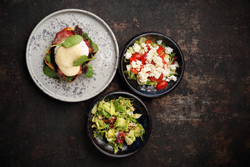 Toast with black pudding, poached egg, bacon and mayonnaise sauce served with a patch of fresh green vegetables. Food, ready dish on a dark background. Suggestion of serving the dish.top view