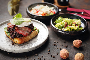 Toast with black pudding, poached egg, bacon and mayonnaise sauce. Food, ready dish on a dark background. Suggestion of serving the dish.