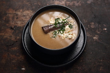  Brown soup with sausage and cream served with herbs. Food, ready dish on a dark background. Suggestion of serving the dish