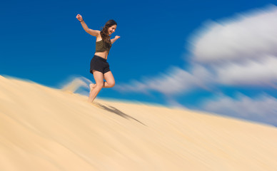 ein M&auml;dchen rennt im Sommer voller Lebensfreude von einer Sandd&uuml;ne und wirbelt dabei Staub auf