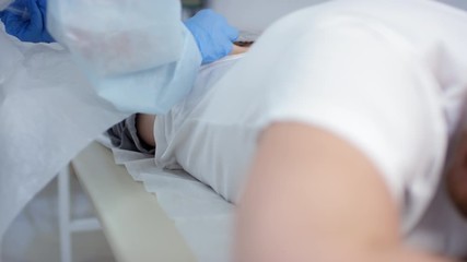 Tracking shot of redhead Caucasian man lying on medical couch with pants below the waist and wincing in pain while nurse giving hum injection into buttock - Powered by Adobe