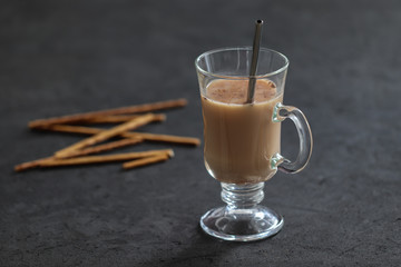 Indian masala tea with milk, spices and cinnamon and biscuits straws on a dark gray background