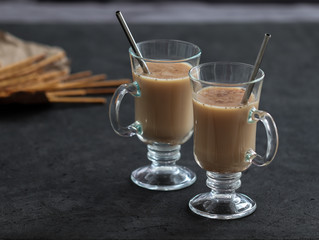 Indian masala tea with milk, spices and cinnamon and biscuits straws on a dark gray background