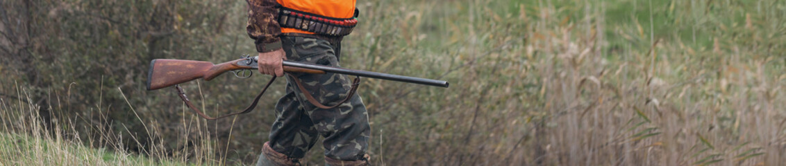 A man with a gun in his hands and an orange vest on a pheasant hunt in a wooded area in cloudy...