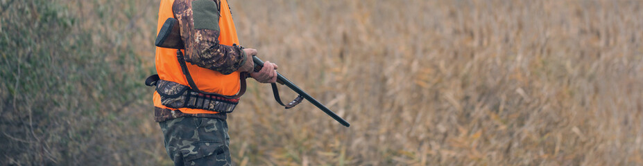 A man with a gun in his hands and an orange vest on a pheasant hunt in a wooded area in cloudy...