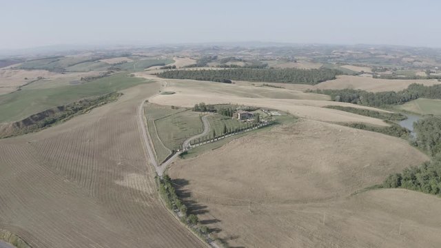 Aerial footage of Tuscany landscape and countryside villa, Val d&rsquo;Orcia, Italy. Golden and green glades, hills, road with cypress trees. Siena. D-log.