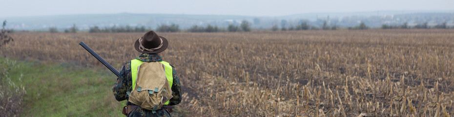 A man with a gun in his hands and an orange vest on a pheasant hunt in a wooded area in cloudy...