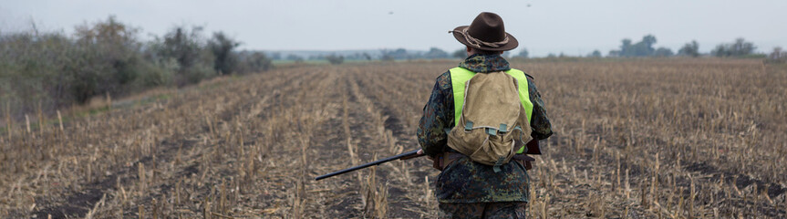 A man with a gun in his hands and an orange vest on a pheasant hunt in a wooded area in cloudy...