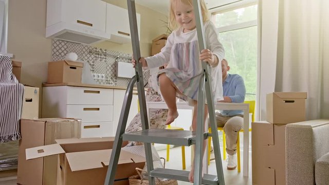 Active Family Group Move in Rent Real Estate. Positive Looking at Relocating or Unpacking of Carton Pack by Playful Family. ittle girl climbs the stairs and looks at the camera.