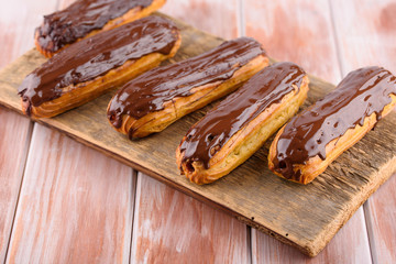 Tasty and beautiful eclairs with chocolate on a wooden board. Appetizing dessert. Party supplies