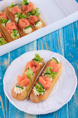 Tasty and beautiful eclairs on a wooden blue board. Appetizing dessert with red fish, cucumber, cheese and greens.