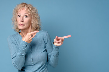 Mature blonde cheerful woman looking aside pointing. Pay attention to this information. Studio shot