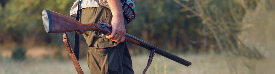 Silhouette of a hunter with a gun in the reeds against the sun, an ambush for ducks with dogs	