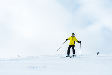 sportsman in helmet holding sticks and skiing on slope with snow in mountains