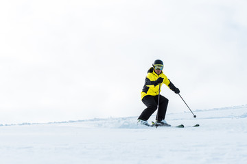 sportsman in helmet and goggles holding sticks and skiing on slope with snow