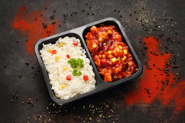 Ready food from the market. Chicken in Mexican sauce with rice. Ready dish in a black container. Composed take-out meal, diet catering. The container on a dark background.