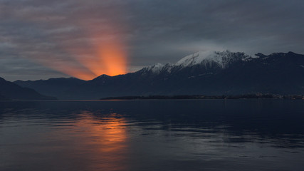 Tramonto sul lago con sole che tramonta e crea cono di luce emergente dalla montagna © fotonaturali