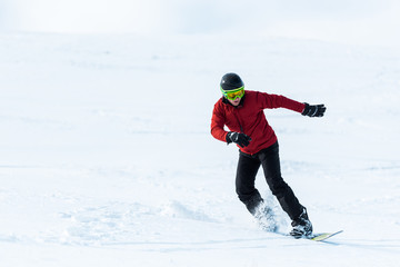 athletic snowboarder in helmet and goggles gesturing while riding on slope outside
