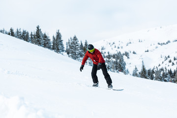 Fototapeta na wymiar athletic snowboarder in helmet riding on slope in mountains