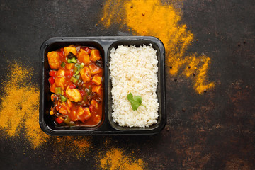 Dietary catering, Chinese chicken with white rice. Ready dish in a black container. Composed take-out meal, diet catering. The container on a dark background.
