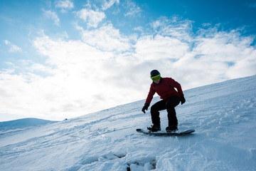 Fototapeta na wymiar athletic snowboarder riding on slope against blue sky in winter