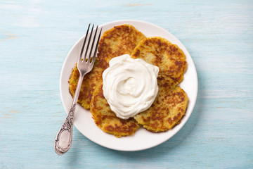 Traditional latkes fritters with sour cream on light blue textured background, top view	