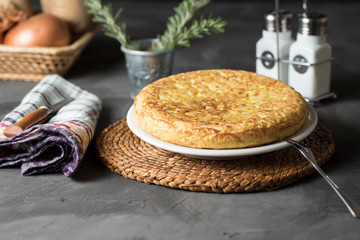 Spanish potato omelette, on a table, next to the necessary ingredients to be cooked and ready to be eaten