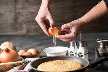 Spanish potato omelette, on a table, next to the necessary ingredients to be cooked and ready to be eaten