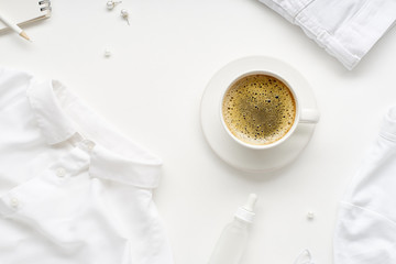 Creative flatlay with monochromatic white clothes and accessories and a cup of coffee on white background. No stain concept