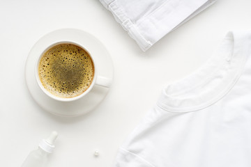 Creative flatlay with monochromatic white clothes and accessories and a cup of coffee on white background. No stain concept