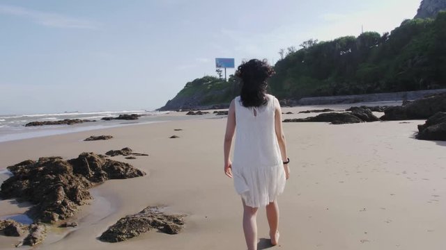 Dark-haired woman, seen from behind, walks on sand beach in Vietnam