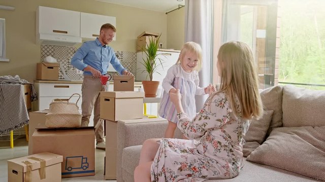 Active Family Group Move in Rent Real Estate. Positive Looking at Relocating or Unpacking of Carton Pack by Playful Family. Little girl jumps on hands to mom. Enjoying Life or Dream