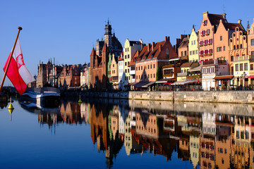 Colorful hanseatic city facades of historic houses close to the Motława river in Gdansk, a port city on the Baltic coast of Poland, in the foreground a polish flag