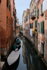 Narrow canal between houses, arched bridge, boats on the water. Venice, Italy.
