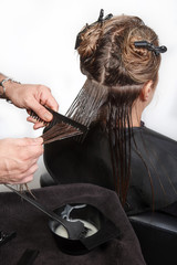 Hairstylist applying mask to hair of her client in beauty hair salon. The process of keratin...