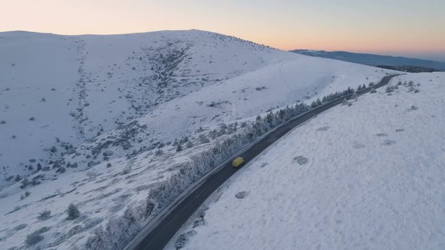 Drone chasing van or truck on mountain road at susnet during winter