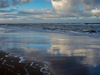 Dramatic blue sky with white clouds reflected on the wet beach at low tide at Noordwijk in The Netherlands