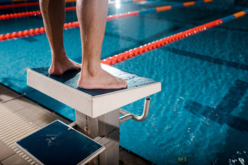 cropped view of sportsman standing on diving block near swimming pool