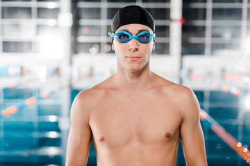 handsome swimmer in goggles and swimming cap looking at camera
